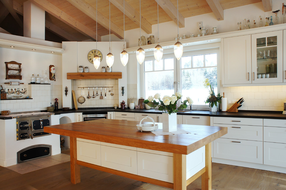 Foto på ett stort lantligt kök, med vita skåp, vitt stänkskydd, rostfria vitvaror, en köksö, skåp i shakerstil, stänkskydd i tunnelbanekakel och ljust trägolv