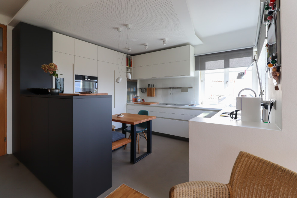 Offene Moderne Küche mit weißen Schränken, Küchenrückwand in Weiß, Glasrückwand, schwarzen Elektrogeräten, Betonboden und grauem Boden in Sonstige