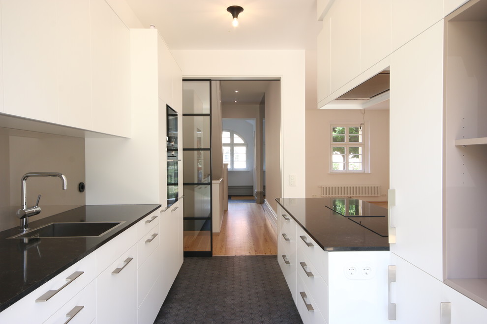 Inspiration för ett mellanstort funkis linjärt kök med öppen planlösning, med en nedsänkt diskho, släta luckor, vita skåp, bänkskiva i kvarts, brunt stänkskydd, glaspanel som stänkskydd, svarta vitvaror, cementgolv, en köksö och grått golv