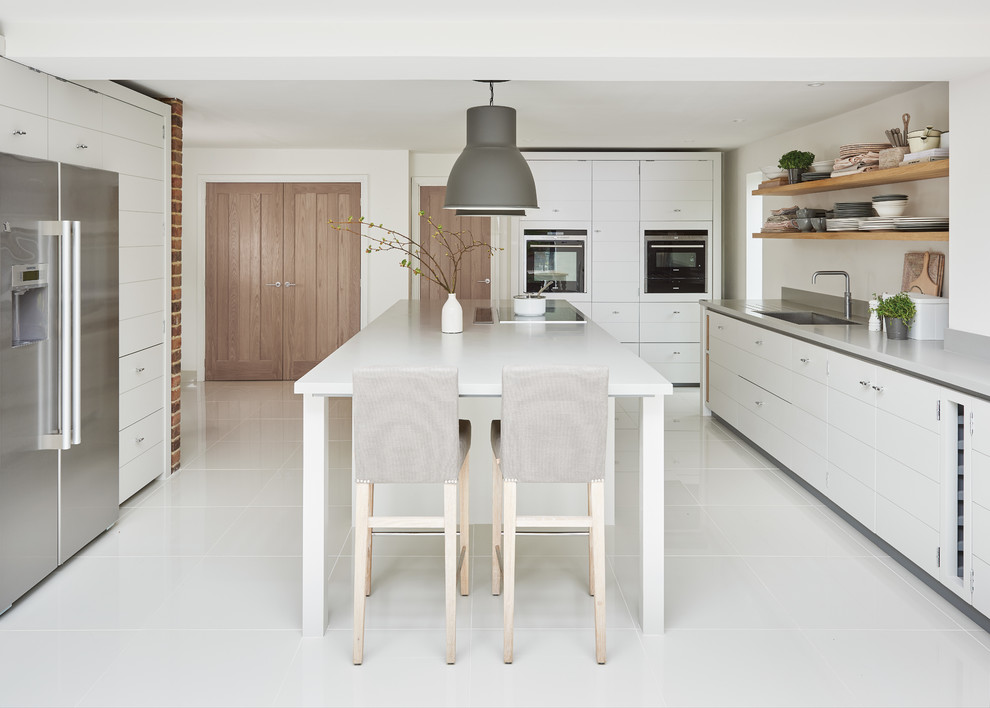 Geräumige Moderne Wohnküche mit flächenbündigen Schrankfronten, weißen Schränken, Küchengeräten aus Edelstahl, Kücheninsel und integriertem Waschbecken in Sonstige