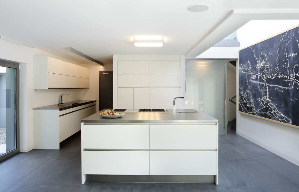 Bild på ett avskilt, stort funkis kök, med en köksö, en enkel diskho, släta luckor, vita skåp, bänkskiva i rostfritt stål och rostfria vitvaror
