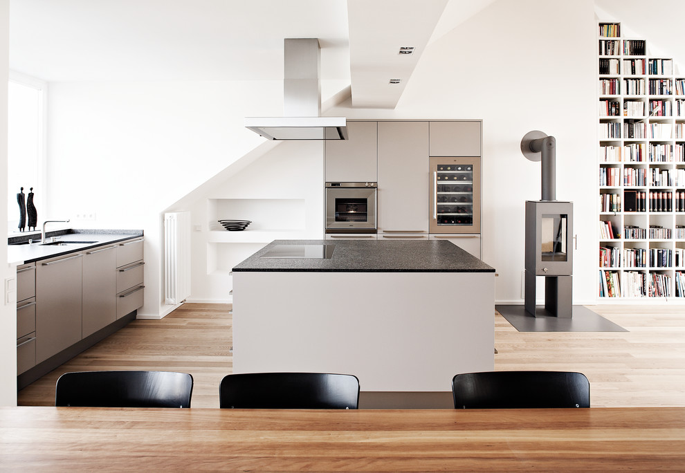 Inspiration for a large contemporary l-shaped open plan kitchen in Other with a submerged sink, flat-panel cabinets, grey cabinets, stainless steel appliances, light hardwood flooring, an island and granite worktops.