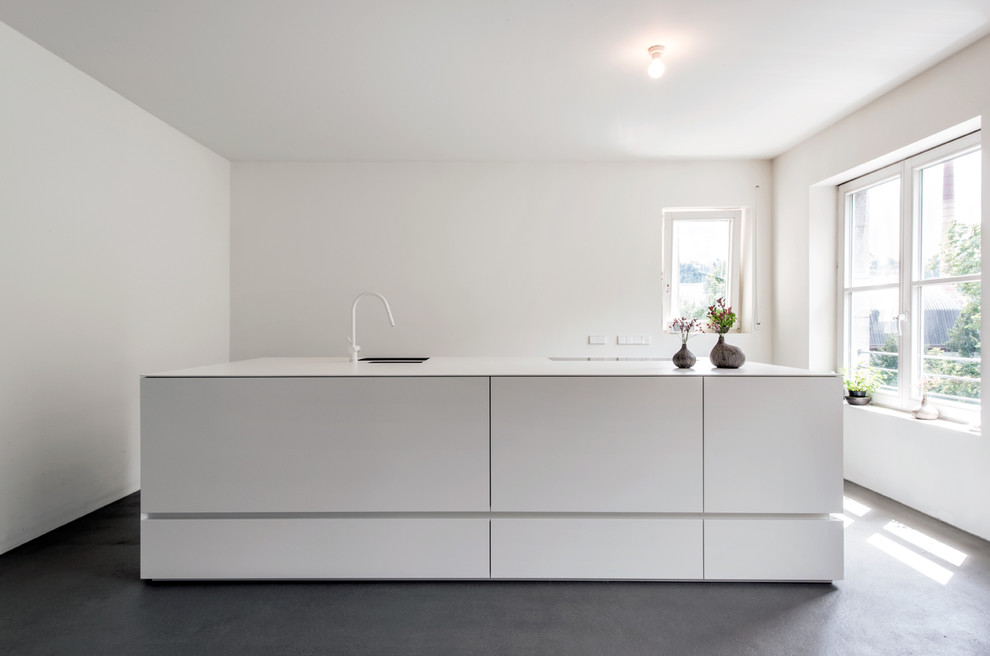 Идея дизайна: маленькая прямая кухня-гостиная в стиле модернизм с накладной мойкой, белыми фасадами, столешницей из оникса, белым фартуком, бетонным полом и островом для на участке и в саду