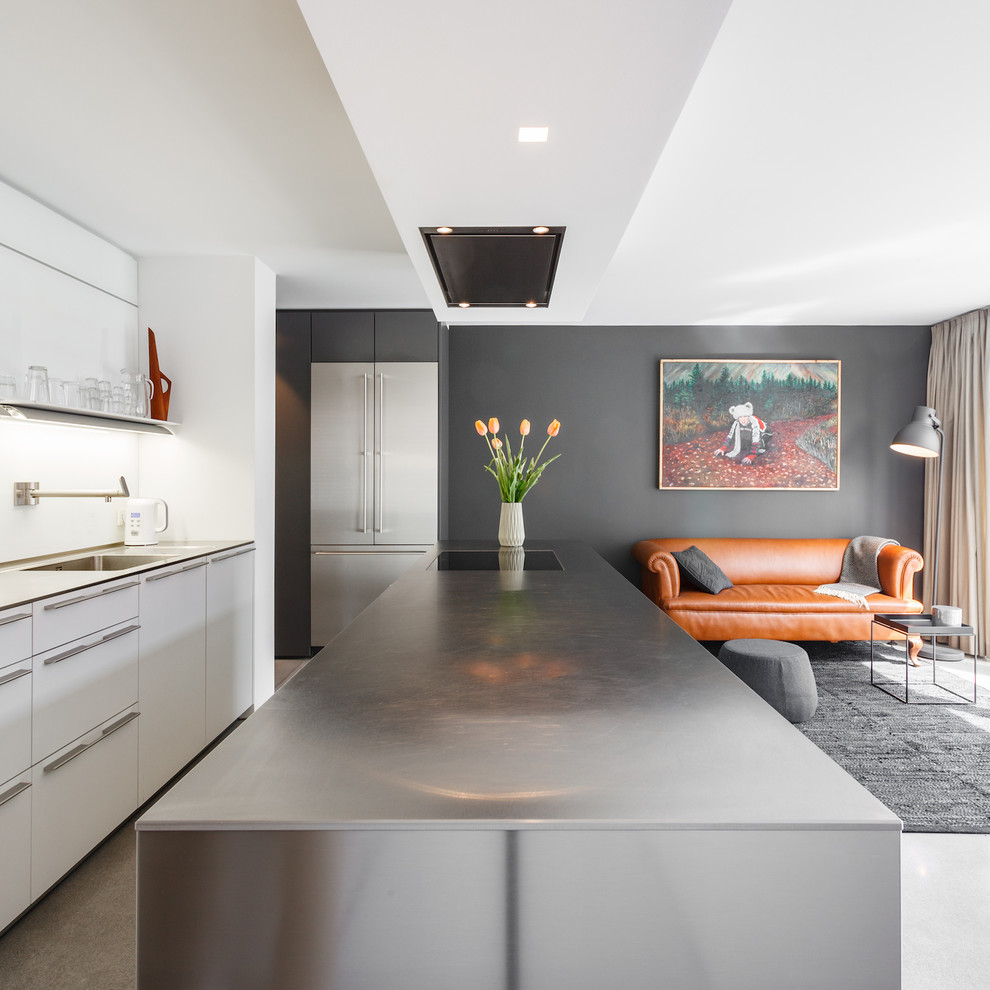 Open concept kitchen - mid-sized contemporary single-wall concrete floor and gray floor open concept kitchen idea in Hamburg with an integrated sink, flat-panel cabinets, white cabinets, stainless steel countertops, white backsplash and an island