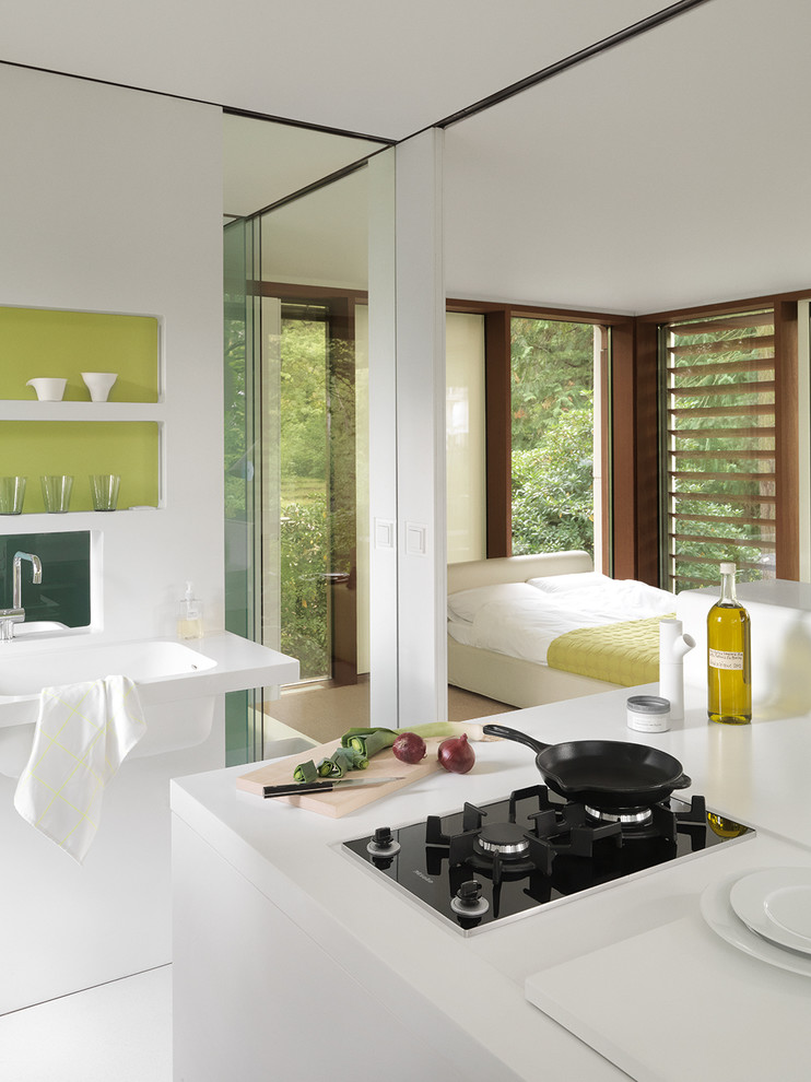 На фото: маленькая кухня-гостиная в современном стиле с зеленым фартуком, монолитной мойкой и белыми фасадами для на участке и в саду с