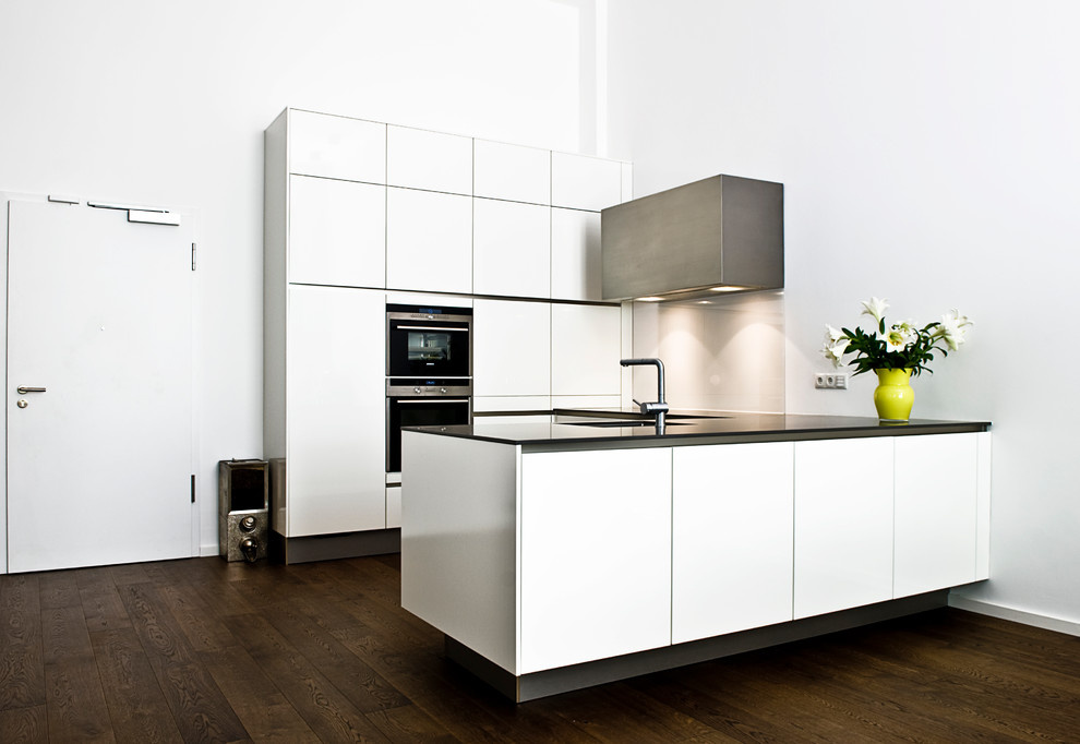 Design ideas for a medium sized contemporary u-shaped open plan kitchen in Hamburg with a single-bowl sink, flat-panel cabinets, white cabinets, white splashback, glass sheet splashback, integrated appliances, dark hardwood flooring and a breakfast bar.