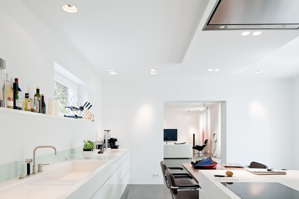 Moderne Wohnküche mit integriertem Waschbecken, flächenbündigen Schrankfronten, weißen Schränken, Küchenrückwand in Weiß, Glasrückwand und Kücheninsel in Köln
