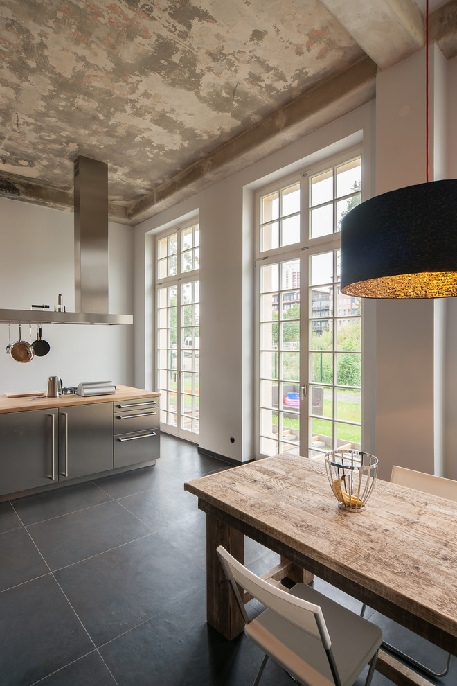 Bild på ett industriellt kök och matrum, med släta luckor, skåp i rostfritt stål, träbänkskiva, skiffergolv och en köksö