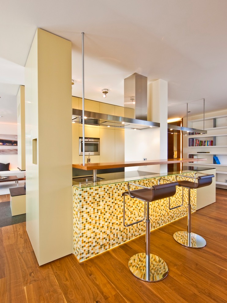 Aménagement d'une cuisine ouverte contemporaine de taille moyenne avec un placard à porte plane, un électroménager en acier inoxydable, un sol en bois brun, des portes de placard jaunes, un évier encastré et une péninsule.