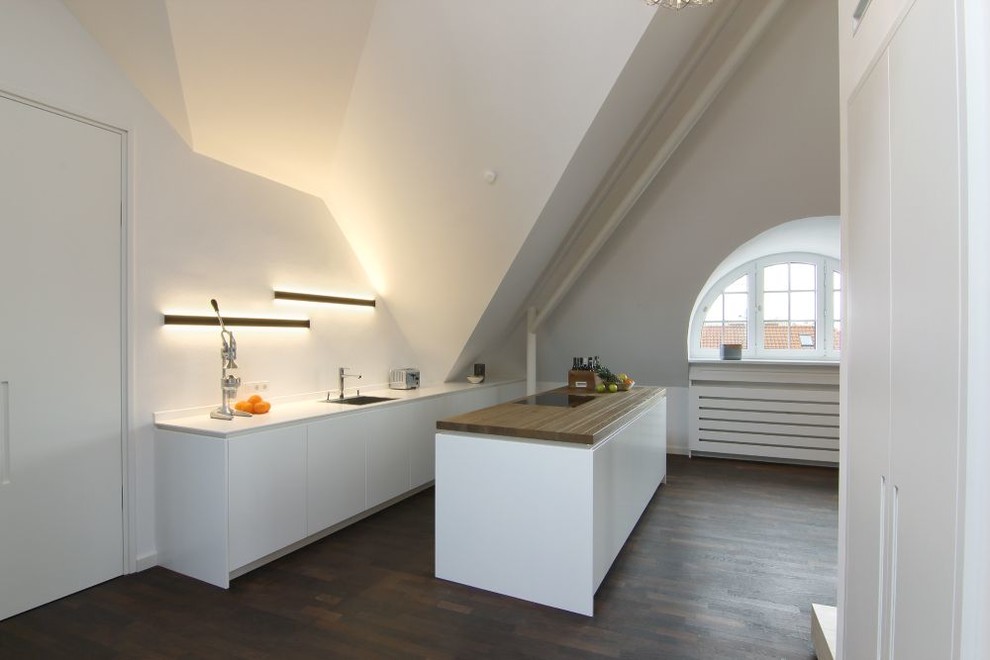 ミュンヘンにある小さなおしゃれなキッチン (ドロップインシンク、フラットパネル扉のキャビネット、白いキャビネット、木材カウンター、白いキッチンパネル、濃色無垢フローリング) の写真