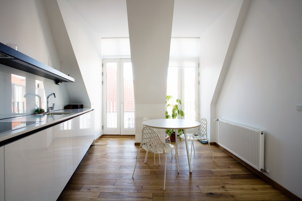 Einzeilige, Mittelgroße Moderne Wohnküche ohne Insel mit Unterbauwaschbecken, flächenbündigen Schrankfronten, weißen Schränken, Küchenrückwand in Weiß, Glasrückwand und dunklem Holzboden in Frankfurt am Main