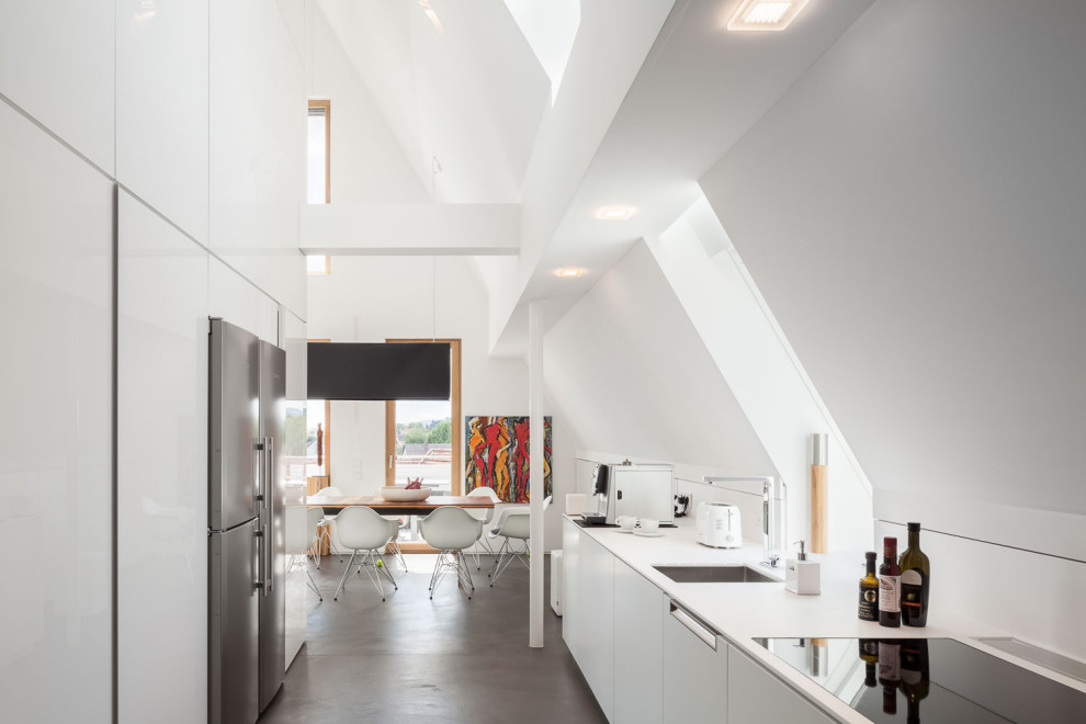 Идея дизайна: прямая кухня-гостиная среднего размера в современном стиле с монолитной мойкой, плоскими фасадами, белыми фасадами, черной техникой, бетонным полом, серым полом и белой столешницей без острова