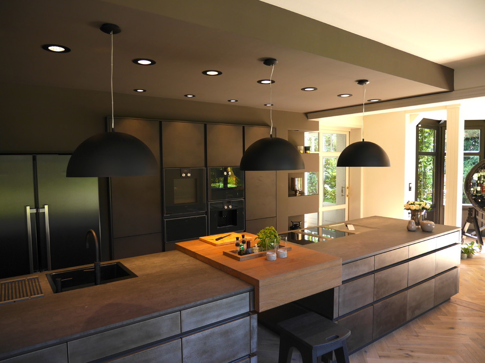 Immagine di un'ampia cucina minimal con lavello da incasso, ante lisce, ante nere, top in superficie solida, elettrodomestici neri, pavimento in legno massello medio, pavimento marrone e top nero