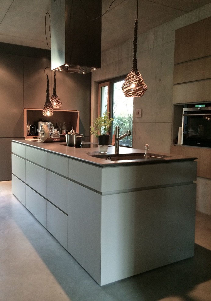 Immagine di un grande cucina con isola centrale minimalista con ante lisce, ante grigie, lavello sottopiano, elettrodomestici neri e pavimento in cemento