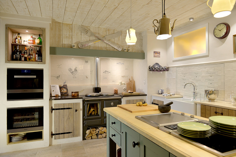 This is an example of a medium sized rural l-shaped open plan kitchen in Dusseldorf with a belfast sink, raised-panel cabinets, light wood cabinets, limestone worktops, black appliances, limestone flooring, an island and beige floors.