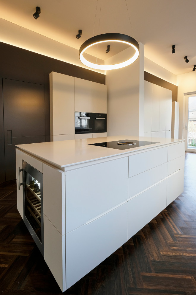 Esempio di una grande cucina minimal con lavello sottopiano, ante lisce, ante marroni, elettrodomestici neri, pavimento in legno massello medio, pavimento marrone e top bianco