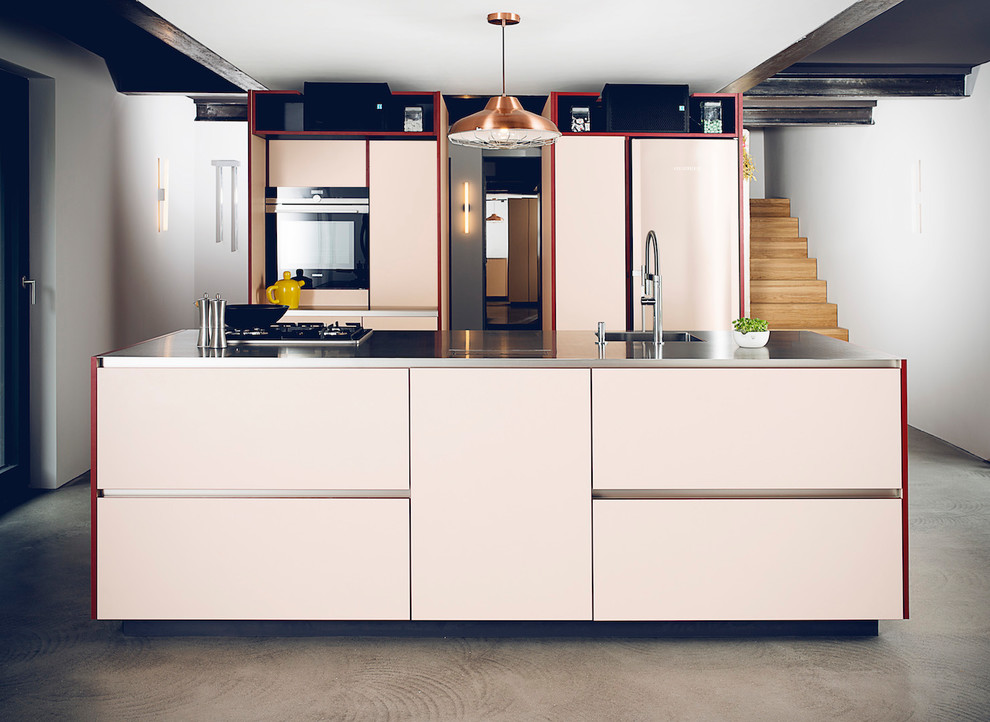 This is an example of a medium sized industrial single-wall open plan kitchen in Dusseldorf with a built-in sink, flat-panel cabinets, stainless steel worktops, black appliances, concrete flooring, an island, grey floors, beige cabinets, beige splashback and grey worktops.