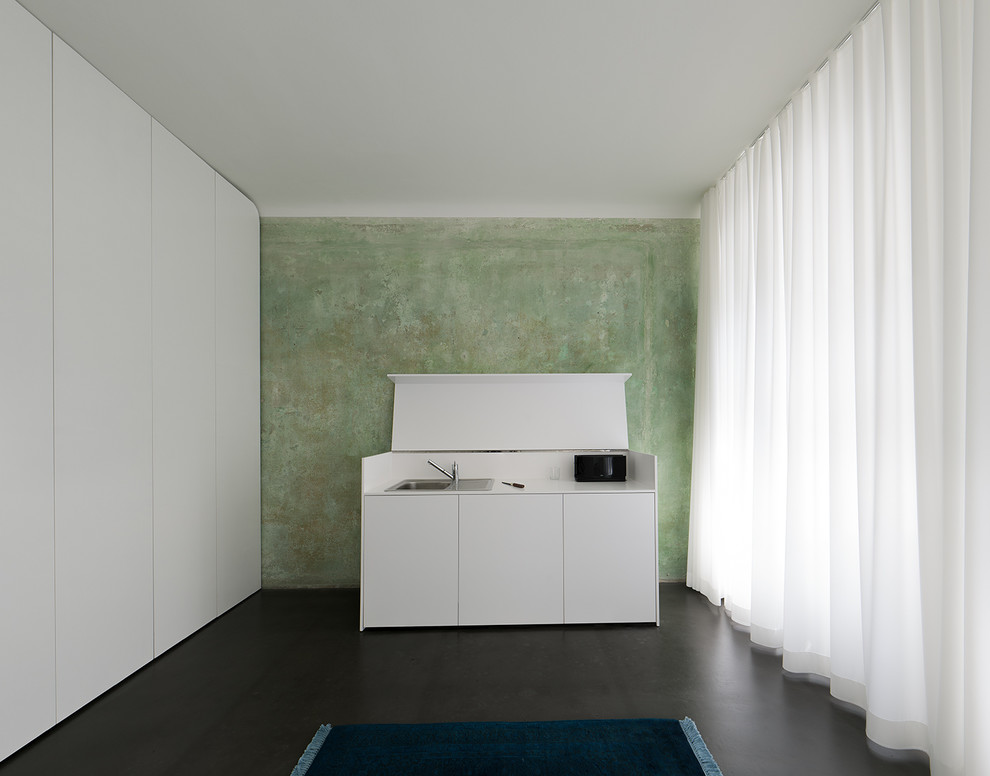 Cette image montre une petite cuisine linéaire design avec un évier posé, un placard à porte plane et des portes de placard blanches.