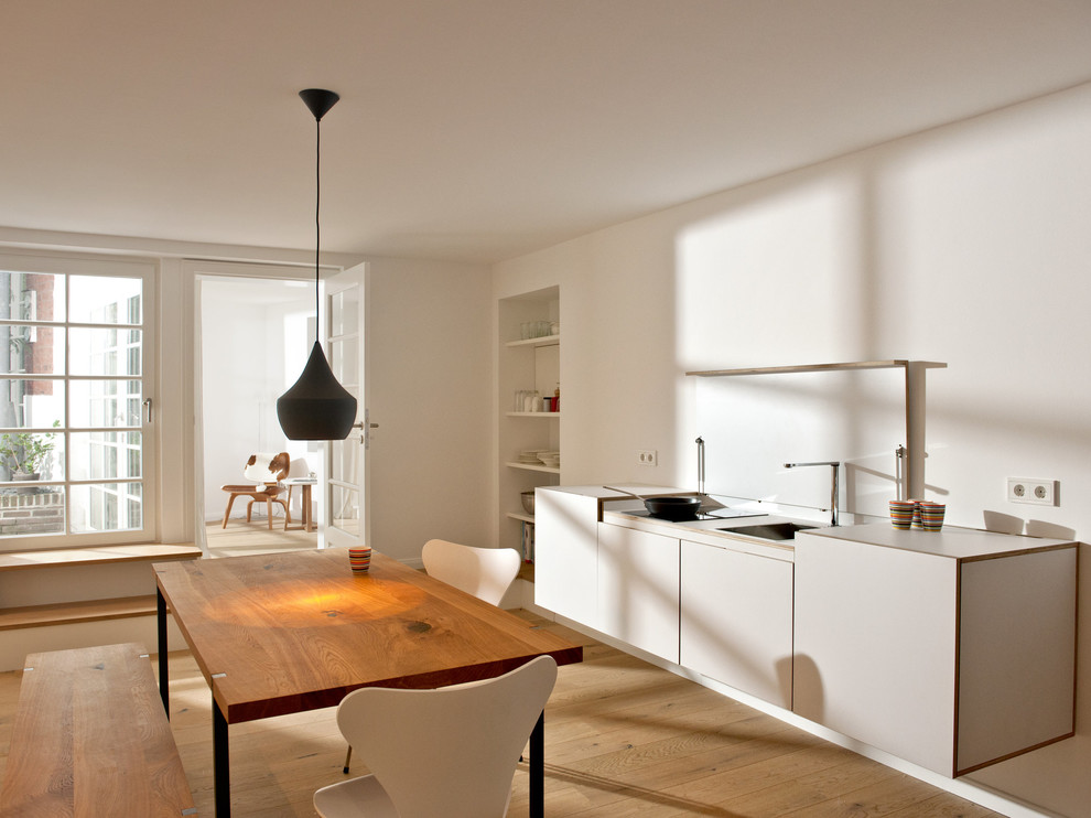 Einzeilige, Kleine Skandinavische Wohnküche ohne Insel mit Einbauwaschbecken, flächenbündigen Schrankfronten, weißen Schränken und hellem Holzboden in Düsseldorf