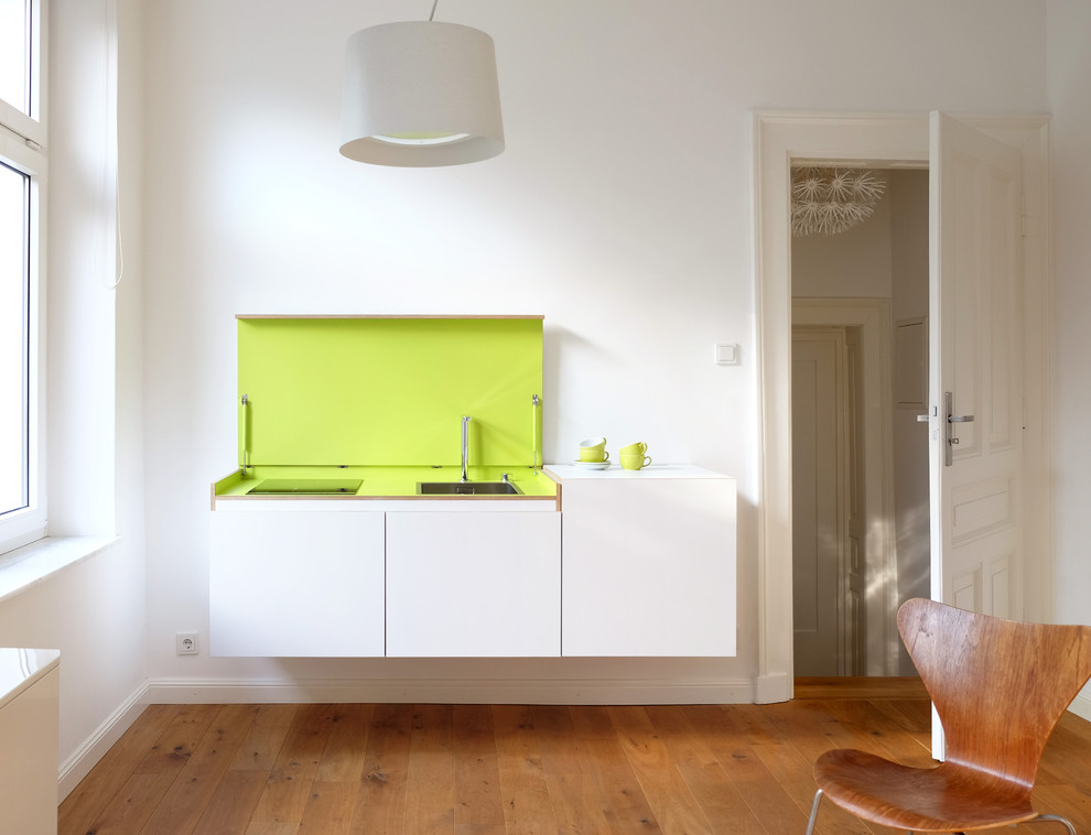 Kleine, Offene, Einzeilige Moderne Küche mit Waschbecken, flächenbündigen Schrankfronten, weißen Schränken, braunem Holzboden und Kücheninsel in Düsseldorf