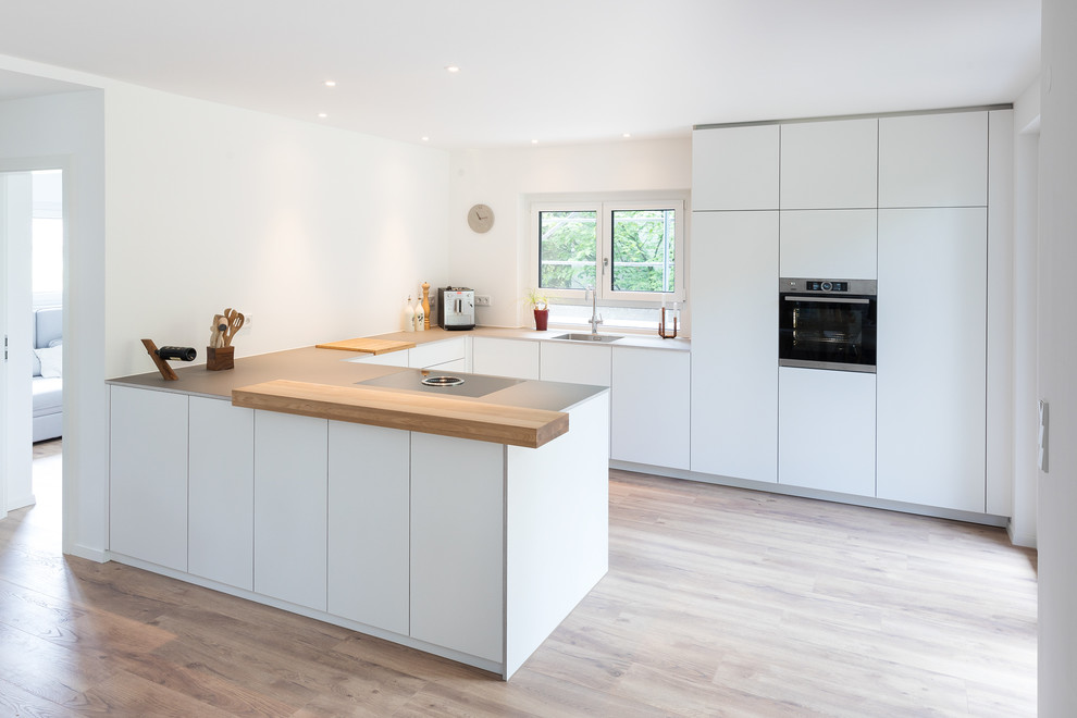 Modern inredning av ett stort grå grått kök, med släta luckor, vita skåp, vitt stänkskydd, rostfria vitvaror, brunt golv, en enkel diskho och mellanmörkt trägolv