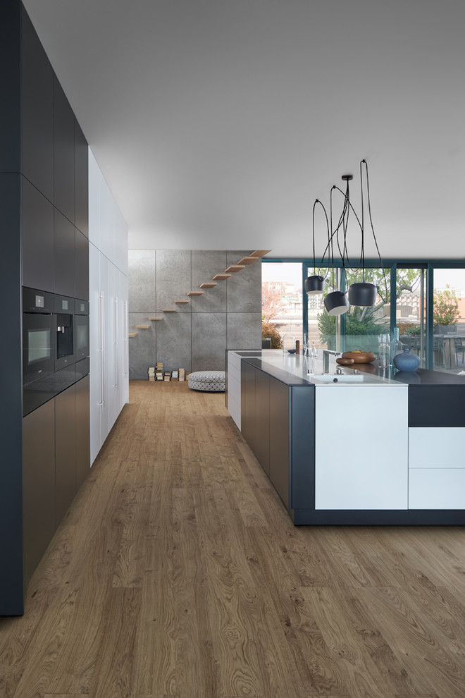 Foto på ett mycket stort funkis kök, med en integrerad diskho, släta luckor, svarta skåp, vitt stänkskydd, stänkskydd i trä, svarta vitvaror, mörkt trägolv, en köksö och brunt golv