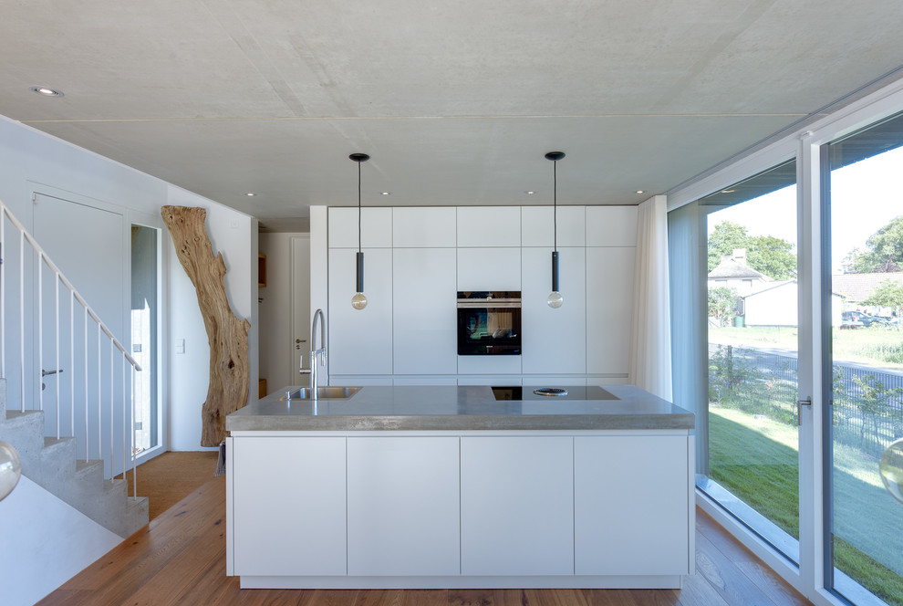 Idéer för ett mellanstort modernt kök med öppen planlösning, med en nedsänkt diskho, släta luckor, vita skåp, bänkskiva i rostfritt stål, rostfria vitvaror, mellanmörkt trägolv och en köksö