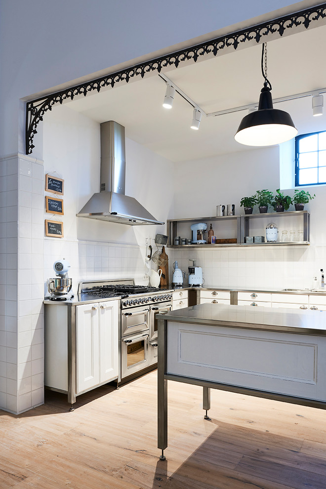 Réalisation d'une cuisine ouverte urbaine en L de taille moyenne avec un plan de travail en granite, une crédence grise, 2 îlots, un évier posé, un placard avec porte à panneau encastré, des portes de placard blanches, un électroménager en acier inoxydable, un sol en bois brun et un sol marron.