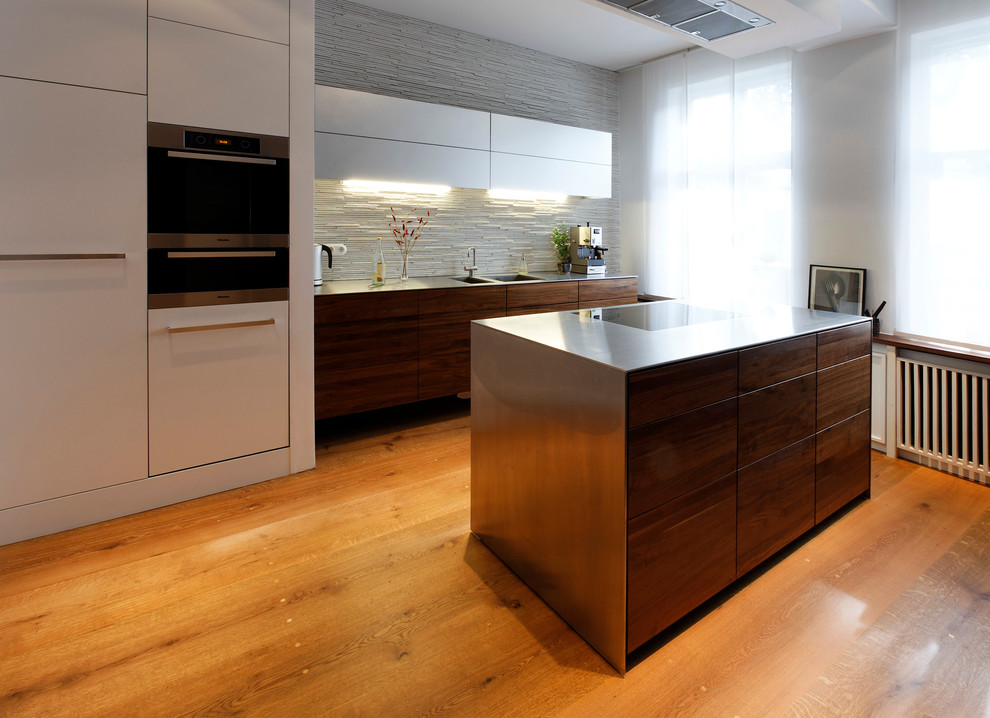 Modern inredning av ett litet linjärt kök med öppen planlösning, med en dubbel diskho, släta luckor, skåp i mörkt trä, bänkskiva i rostfritt stål, vitt stänkskydd, stänkskydd i stenkakel, rostfria vitvaror, målat trägolv och beiget golv
