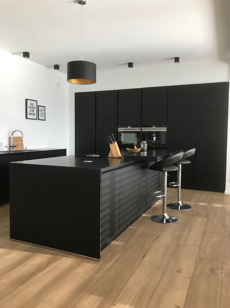 Immagine di una cucina contemporanea di medie dimensioni con lavello da incasso, ante lisce, ante nere, elettrodomestici neri, pavimento in legno verniciato, penisola e pavimento marrone