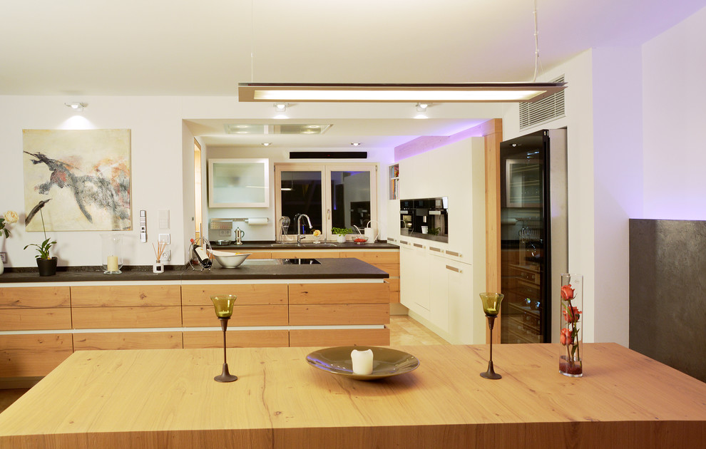 Immagine di un'ampia cucina abitabile minimal con ante lisce, ante in legno chiaro, paraspruzzi bianco, penisola, lavello a doppia vasca e elettrodomestici neri