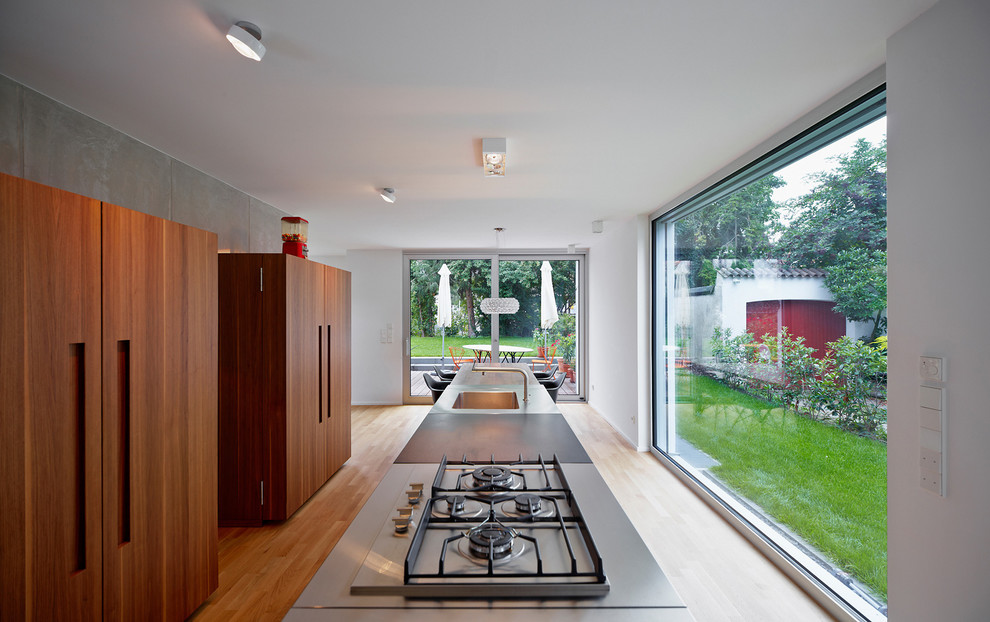 Foto på ett stort funkis kök och matrum, med en integrerad diskho, en köksö, bänkskiva i rostfritt stål, grått stänkskydd, mellanmörkt trägolv, släta luckor och skåp i mörkt trä