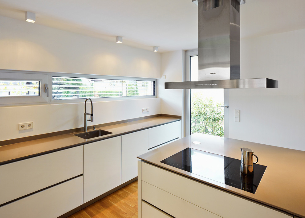 Foto di un cucina con isola centrale minimal chiuso e di medie dimensioni con lavello sottopiano, ante lisce, ante bianche e pavimento in legno massello medio