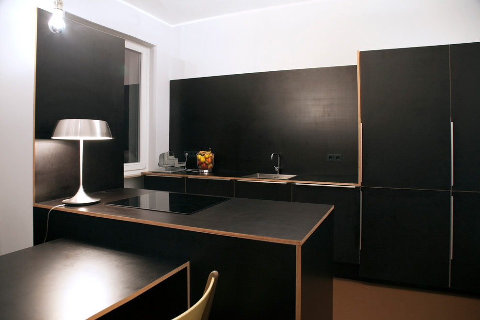 Diseño de cocina actual de tamaño medio abierta con fregadero encastrado, armarios con paneles lisos, puertas de armario negras, salpicadero negro, electrodomésticos con paneles y península