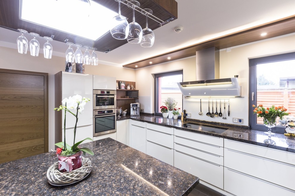 This is an example of a large contemporary kitchen in Other with flat-panel cabinets, white cabinets, stainless steel appliances, an island and black splashback.