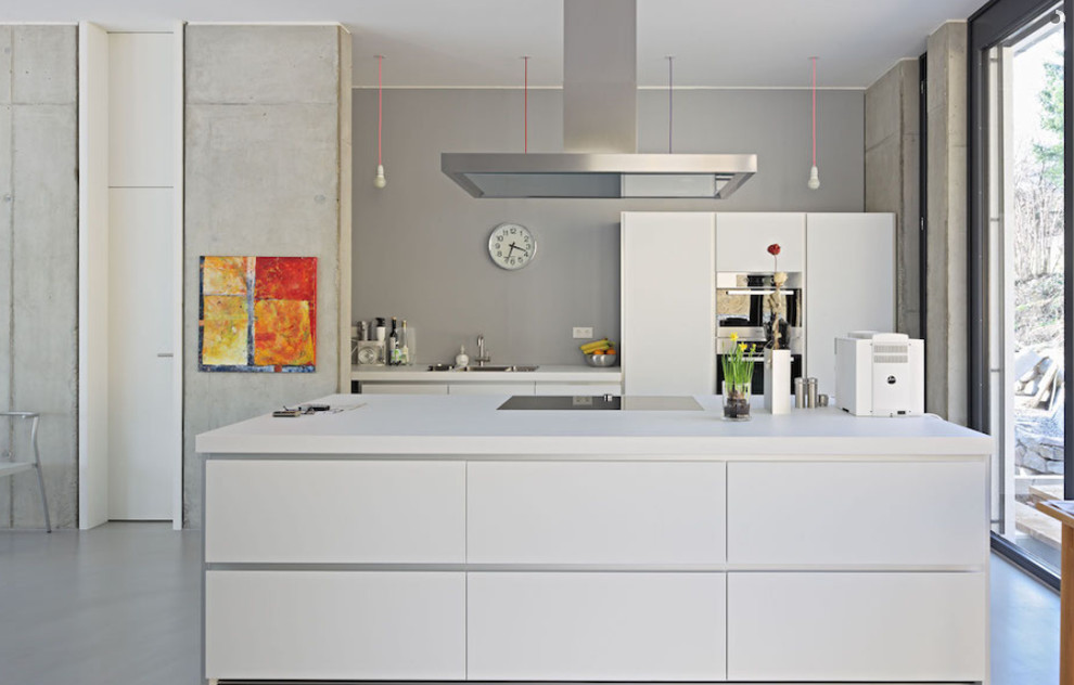 Foto på ett stort funkis kök med öppen planlösning, med en nedsänkt diskho, släta luckor, vita skåp, grått stänkskydd, rostfria vitvaror, en köksö och betonggolv