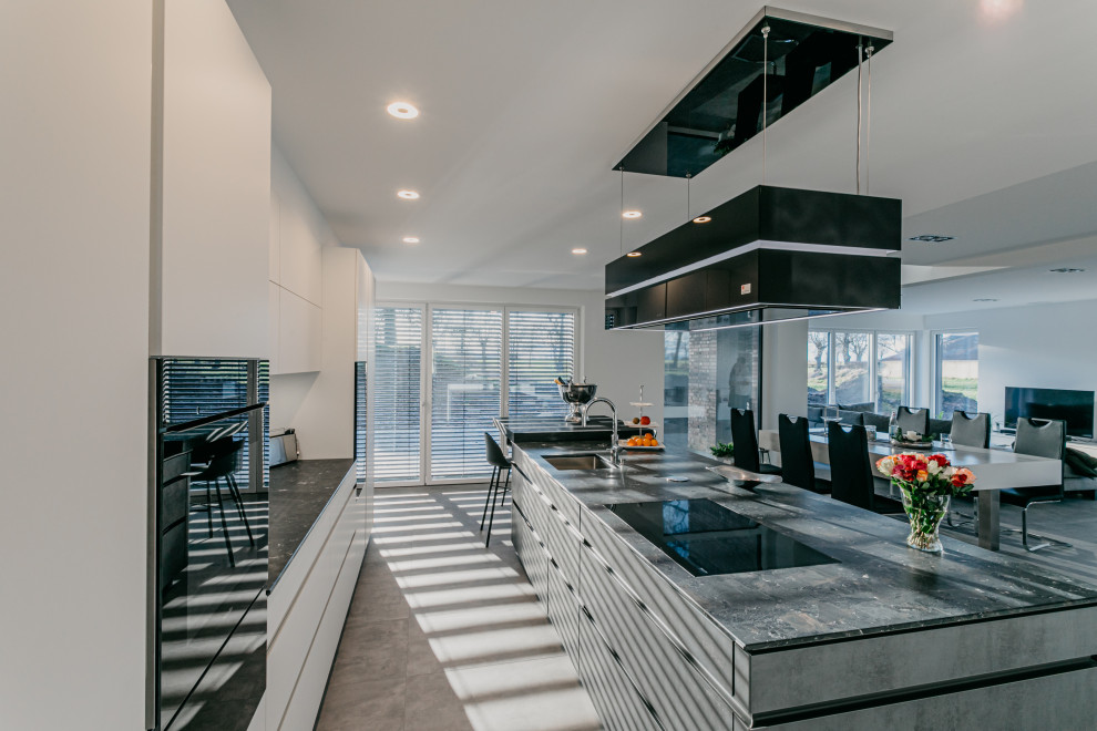 Large contemporary galley open plan kitchen in Cologne with a submerged sink, flat-panel cabinets, granite worktops, black appliances, concrete flooring, an island, grey floors and brown worktops.
