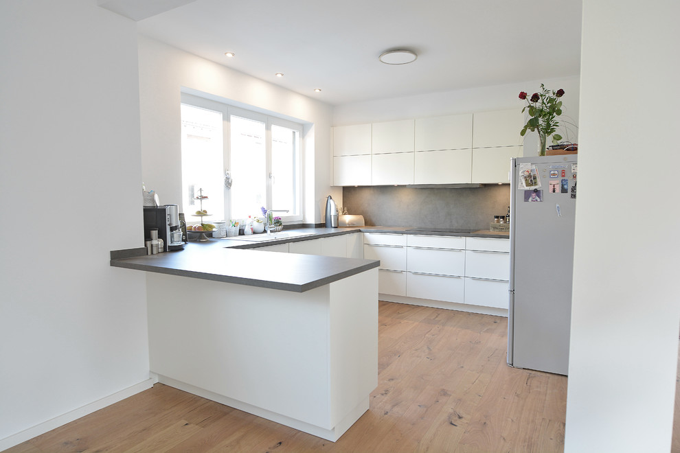 Photo of an expansive modern u-shaped open plan kitchen in Frankfurt with a built-in sink, flat-panel cabinets, white cabinets, grey splashback, stainless steel appliances, light hardwood flooring, no island, wood worktops, wood splashback and brown floors.