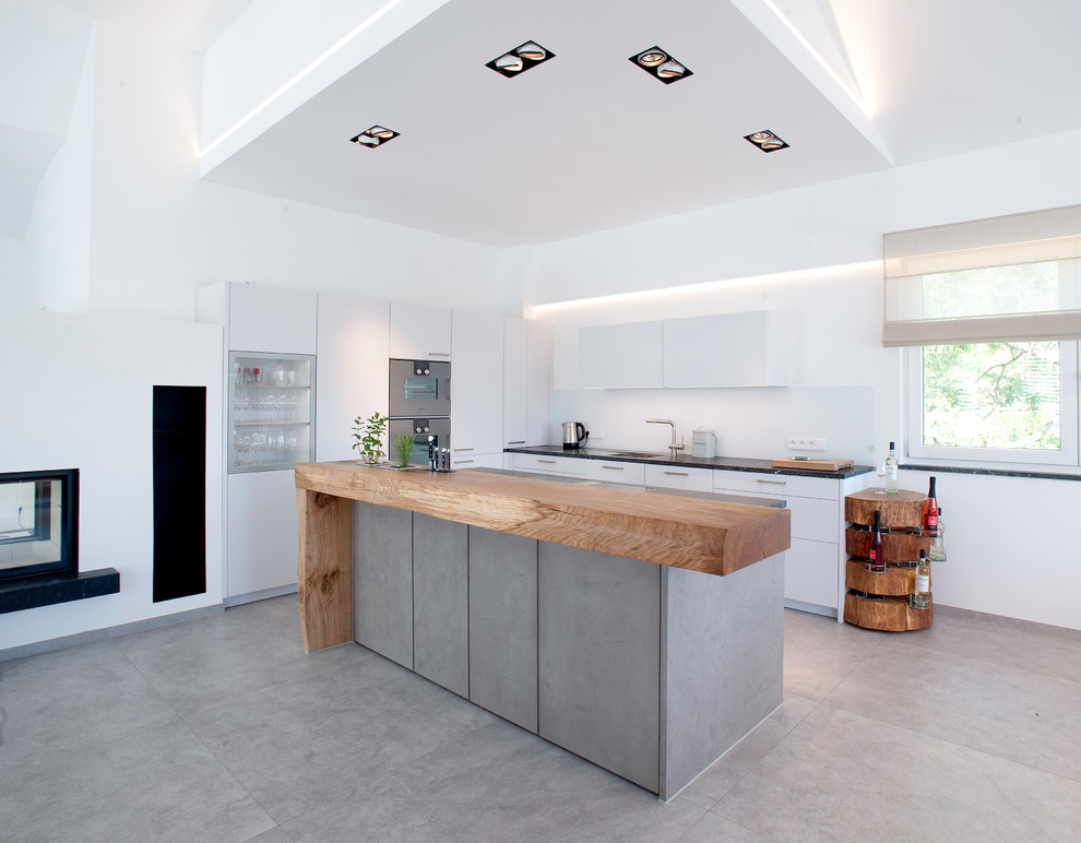 Foto på ett funkis svart kök, med en enkel diskho, släta luckor, vita skåp, rostfria vitvaror, betonggolv, en köksö och grått golv