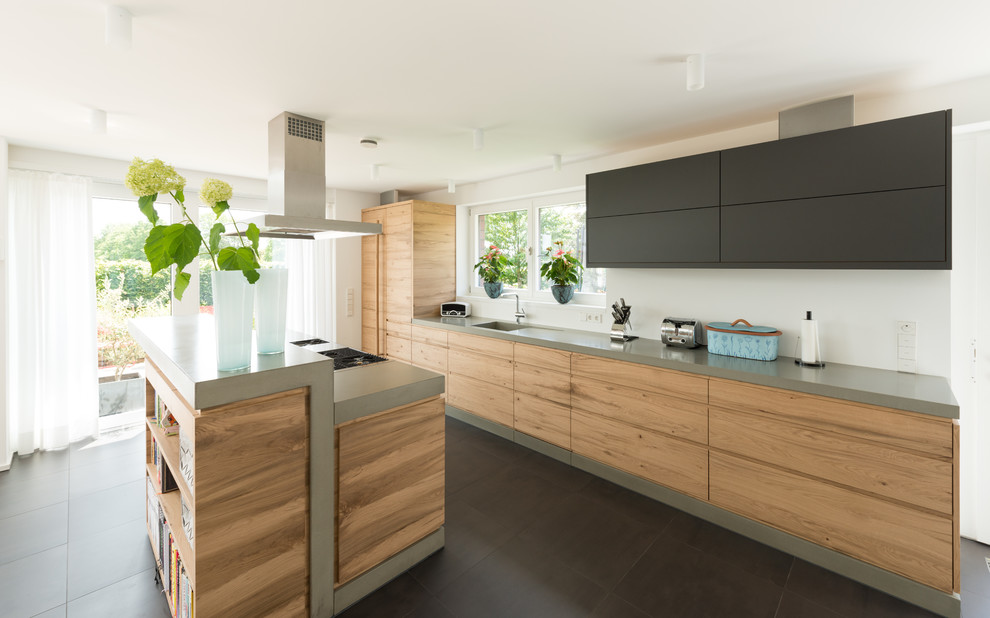 Inspiration for a mid-sized contemporary single-wall ceramic tile and gray floor open concept kitchen remodel in Other with a single-bowl sink, flat-panel cabinets, light wood cabinets, concrete countertops, white backsplash, black appliances and an island