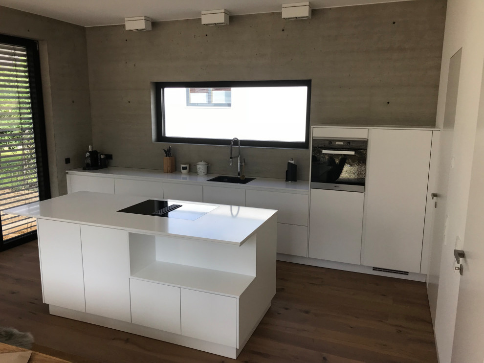 Idee per un cucina con isola centrale minimal con ante bianche, paraspruzzi grigio, pavimento in laminato, pavimento marrone e top bianco