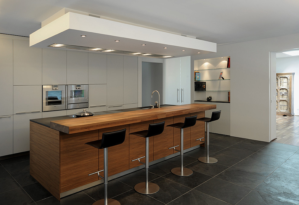 Modern inredning av ett stort kök med öppen planlösning, med en enkel diskho, släta luckor, vita skåp, integrerade vitvaror, skiffergolv och en köksö