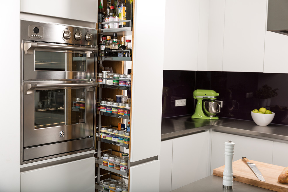Bild på ett mellanstort industriellt kök, med en integrerad diskho, släta luckor, vita skåp, flerfärgad stänkskydd, glaspanel som stänkskydd, rostfria vitvaror, mörkt trägolv och en köksö