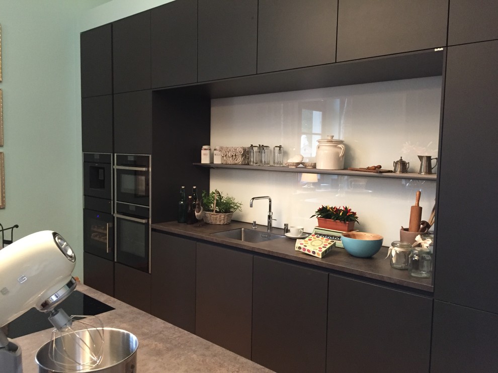 Esempio di una cucina design di medie dimensioni con ante lisce, ante nere, top in superficie solida, paraspruzzi multicolore, paraspruzzi con lastra di vetro, elettrodomestici neri e pavimento in legno massello medio