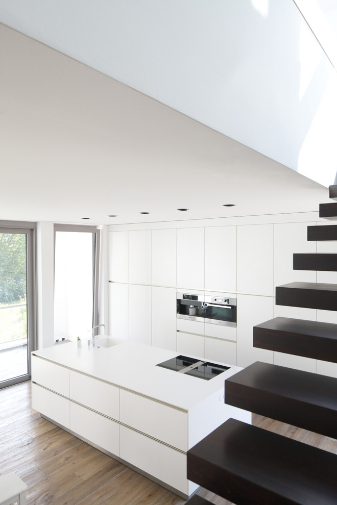 Foto på ett stort funkis linjärt kök och matrum, med släta luckor, vita skåp, rostfria vitvaror, en köksö och ljust trägolv