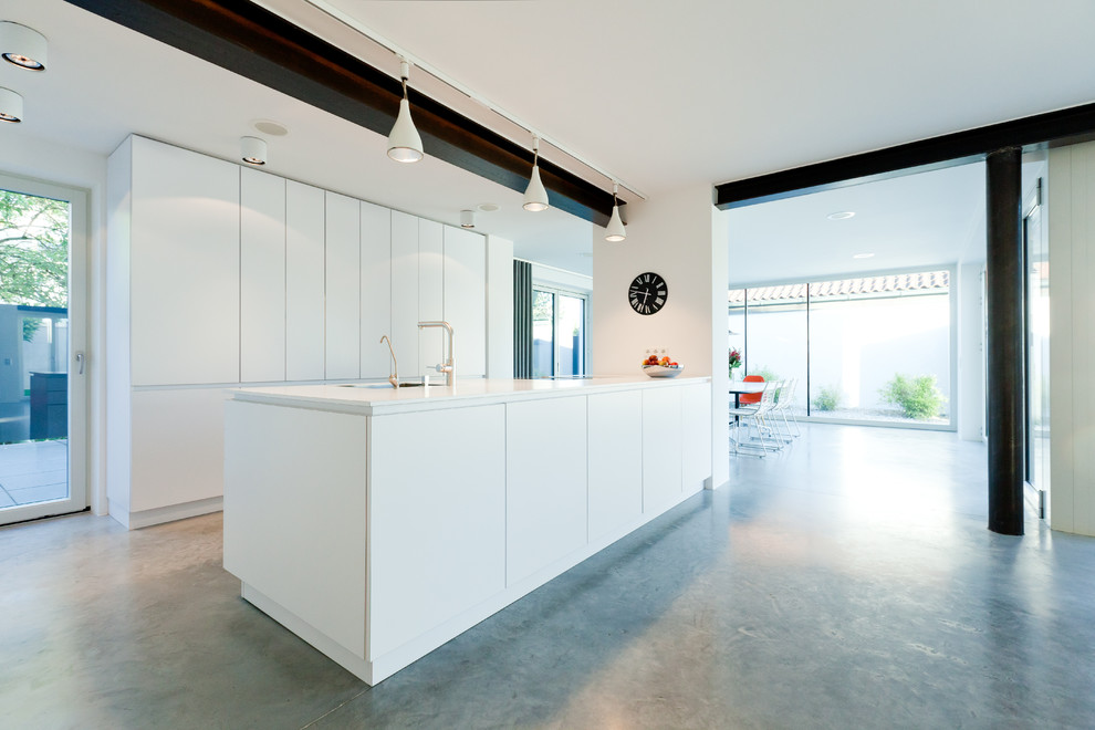 Aménagement d'une cuisine ouverte linéaire industrielle de taille moyenne avec un placard à porte plane, des portes de placard blanches, sol en béton ciré, îlot et un sol gris.