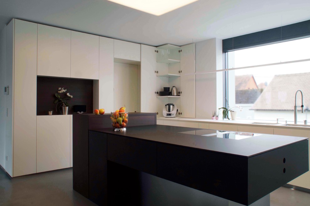 Photo of a medium sized modern l-shaped kitchen/diner in Frankfurt with a double-bowl sink, flat-panel cabinets, white cabinets, composite countertops, white splashback, glass sheet splashback, white appliances, concrete flooring, an island, grey floors and black worktops.