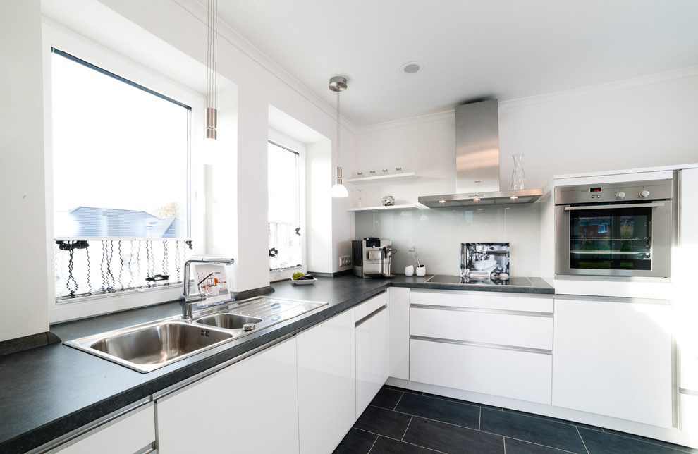 Design ideas for a medium sized contemporary l-shaped enclosed kitchen in Hamburg with an integrated sink, white cabinets, laminate countertops, beige splashback, glass tiled splashback, stainless steel appliances, slate flooring and black floors.