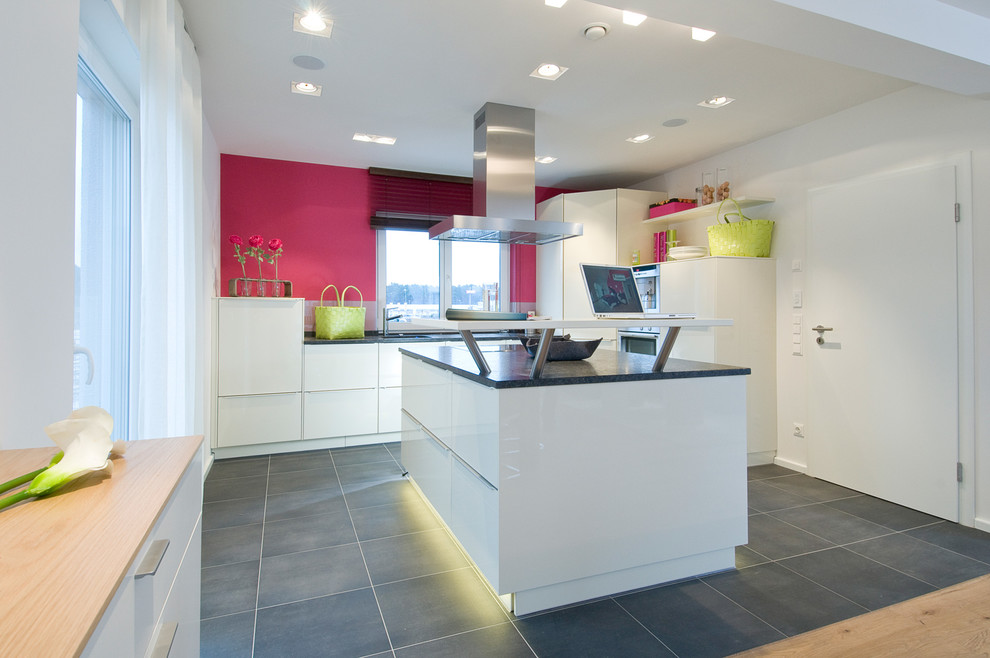 Design ideas for a medium sized contemporary grey and pink l-shaped open plan kitchen in Nuremberg with flat-panel cabinets, white cabinets, granite worktops, pink splashback, porcelain flooring, an island, grey floors, black worktops, an integrated sink and stainless steel appliances.