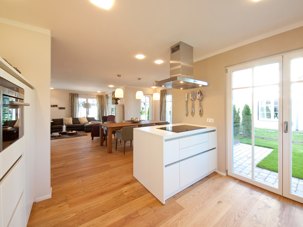This is an example of a large contemporary l-shaped open plan kitchen in Munich with a built-in sink, flat-panel cabinets, white cabinets, wood worktops, brown splashback, wood splashback, stainless steel appliances, medium hardwood flooring, a breakfast bar, brown floors and white worktops.